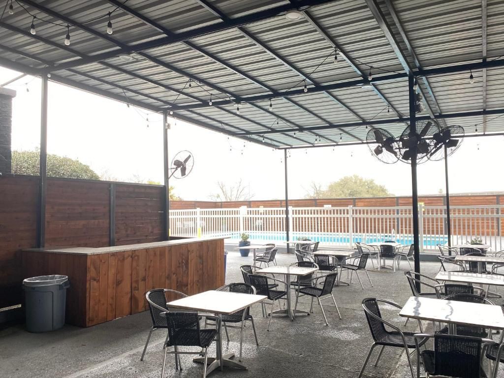 Outdoor patio with tables, chairs, and a pool in the background. Covered with a metal roof and fans.