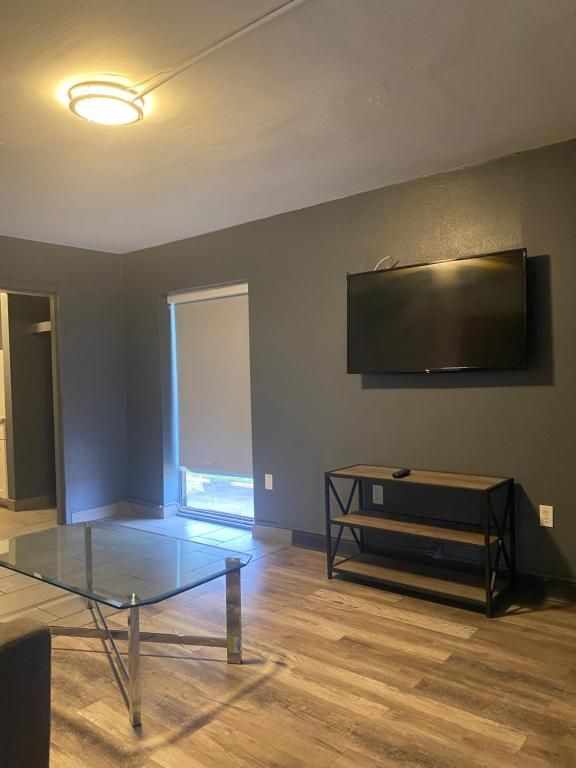 Living room with gray walls, TV, glass coffee table, and wood-look flooring.