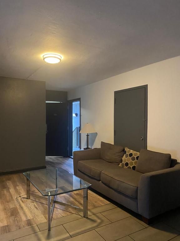 Living room with brown sofa, glass coffee table, and open entry door.