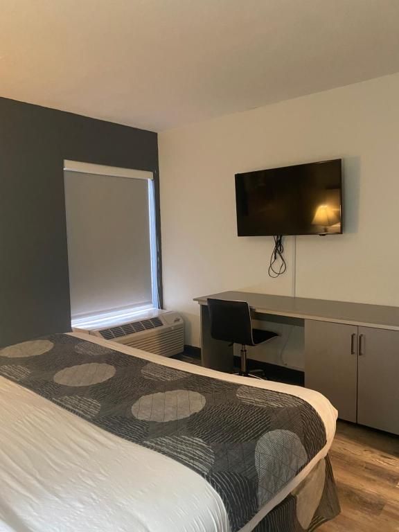 Bedroom with bed, desk, TV, and window with shade. Walls are gray and white.