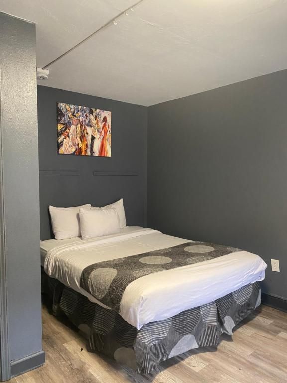A small, gray-walled hotel room with a bed featuring gray patterned bedding, a colorful wall art.