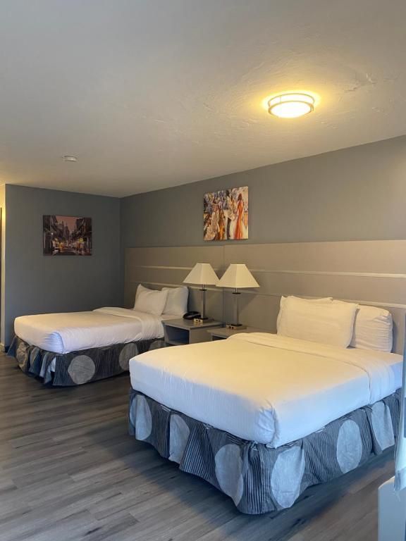 Two beds in a hotel room, gray walls, light wood-look floors. Beds have white linens, blue/white skirt.