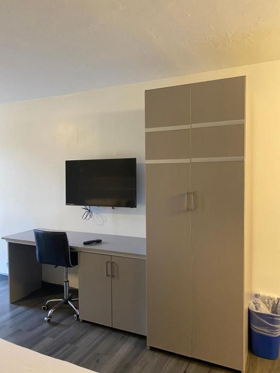 Desk with TV and wardrobe in a room with light-colored walls and a blue trash can.