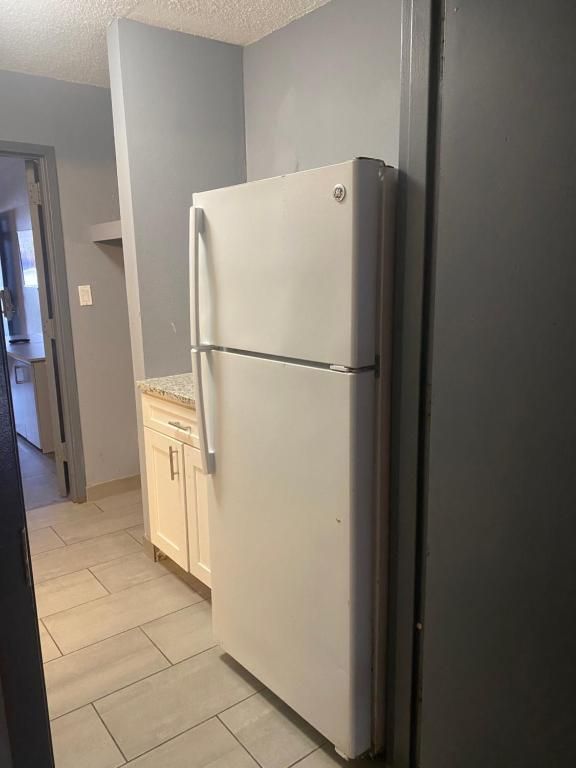 White refrigerator in a kitchen alcove with light wood cabinets and gray walls.