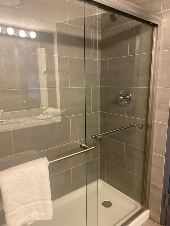 Shower with sliding glass doors, stainless steel handle, gray tile walls. A white towel hangs on the door.