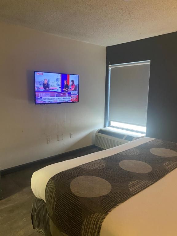 Hotel room with a bed, TV playing news, and a window with a closed blind.