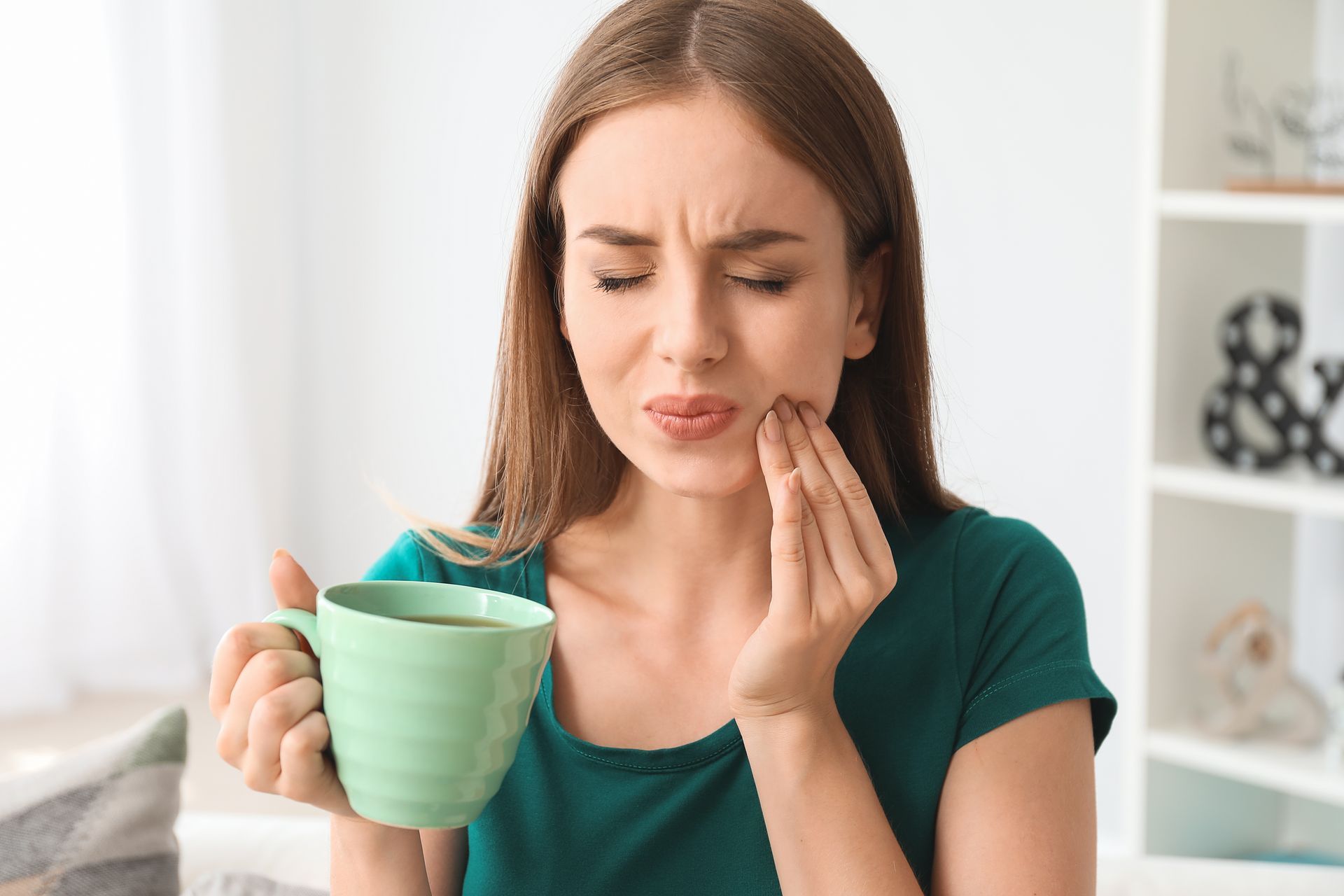 A woman is holding a cup of coffee and having a toothache.