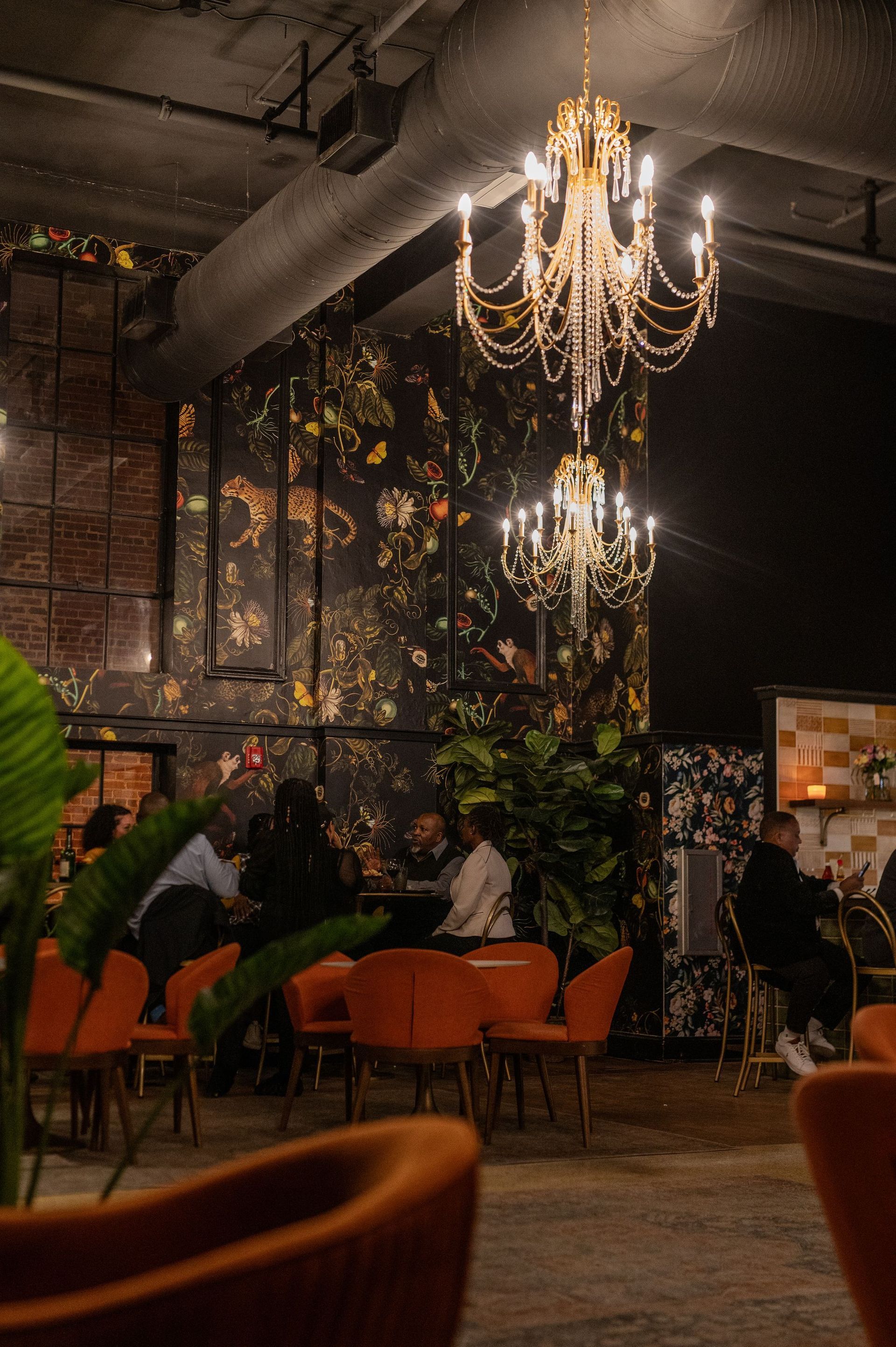 A group of people are sitting at tables in a restaurant with a chandelier hanging from the ceiling.