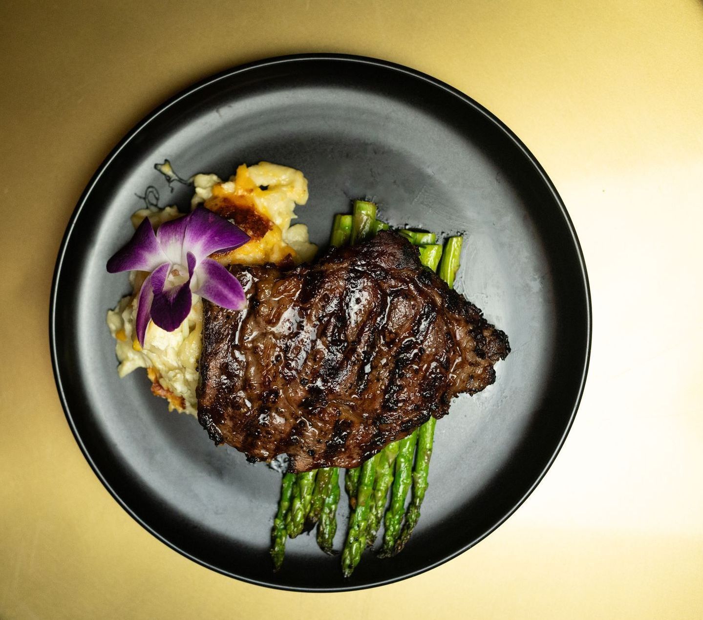 A black plate topped with steak asparagus and mashed potatoes