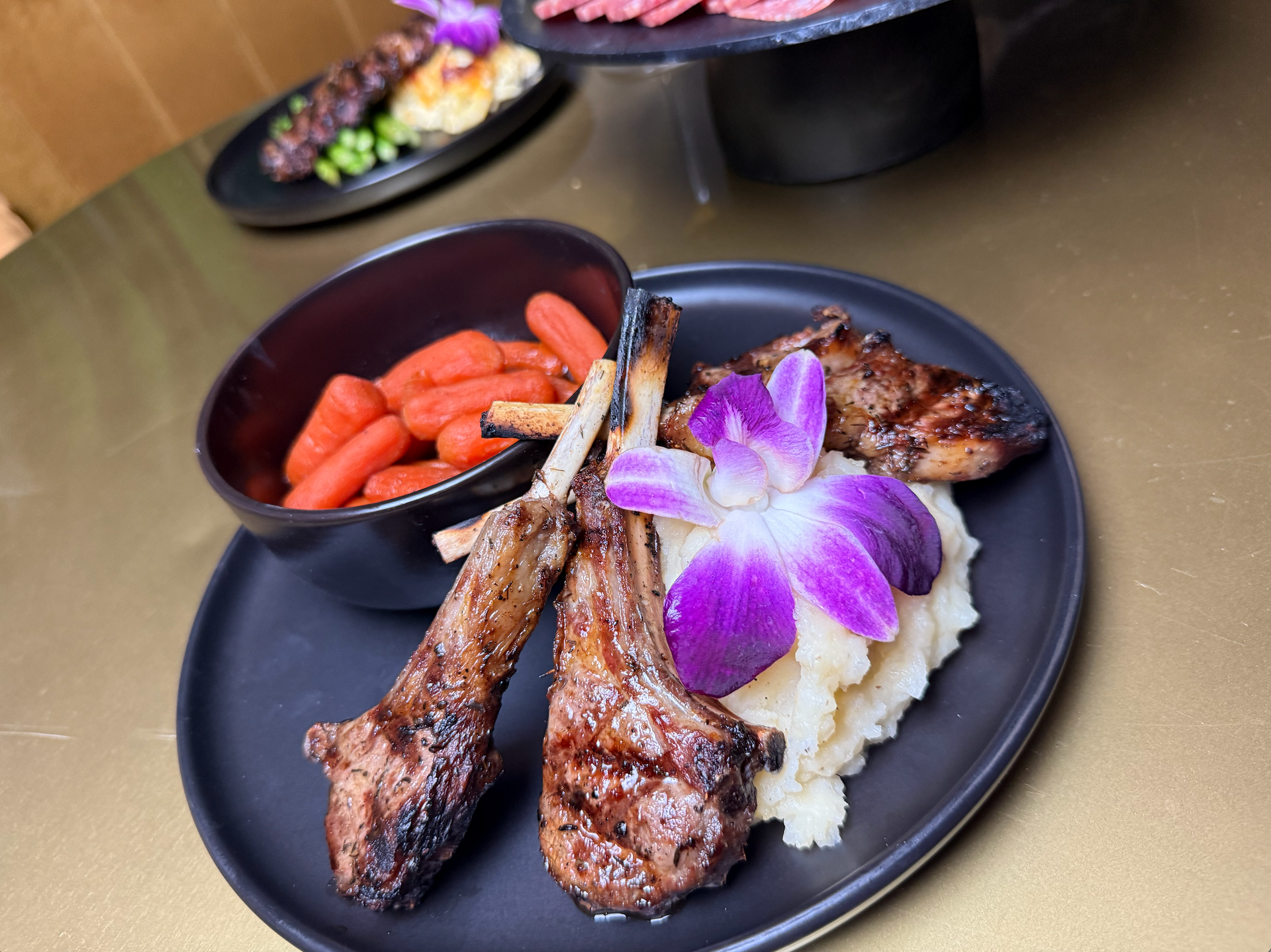 A plate of lamb chops with mashed potatoes and carrots on a table.