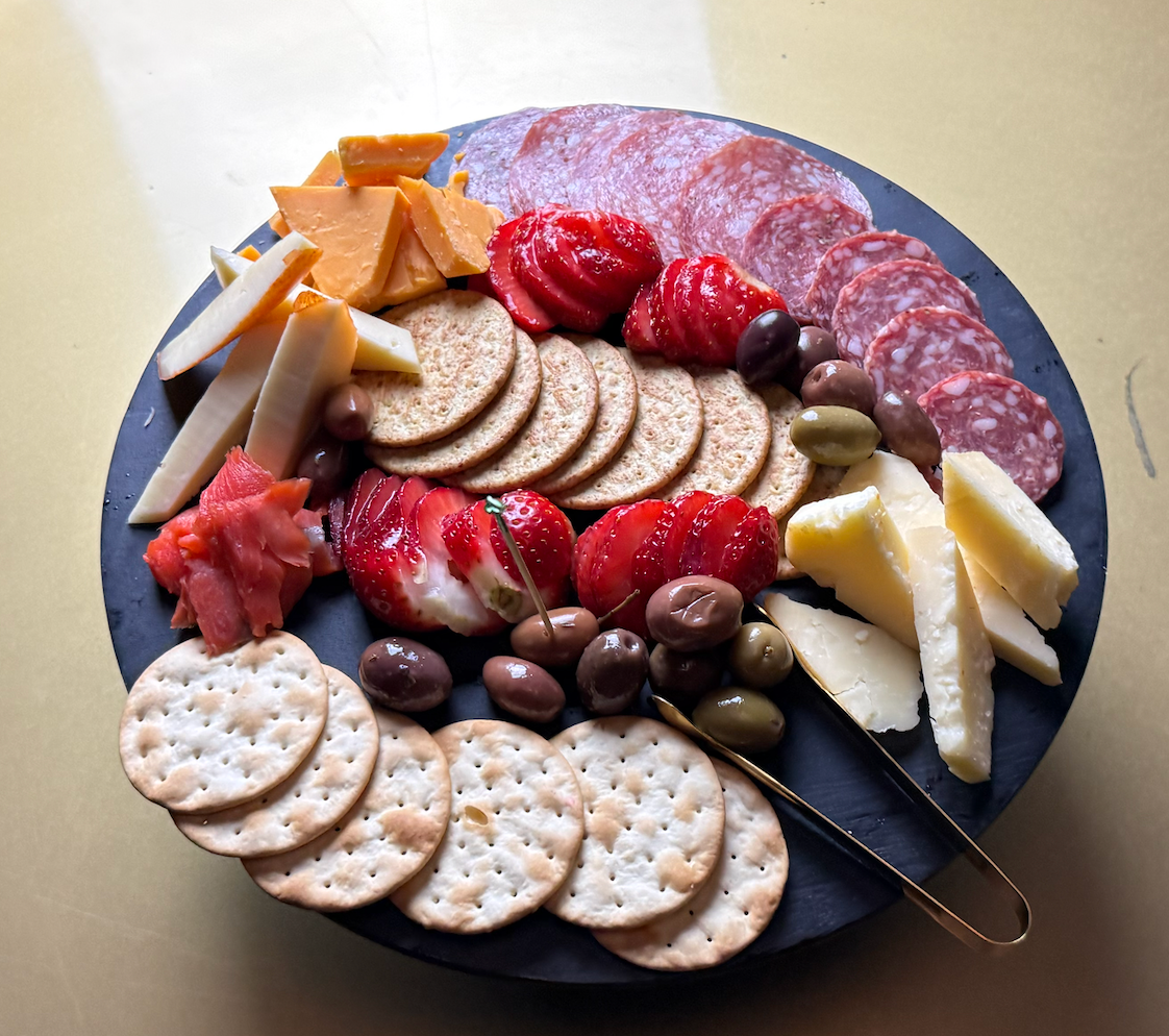 A plate of food with crackers strawberries olives and cheese