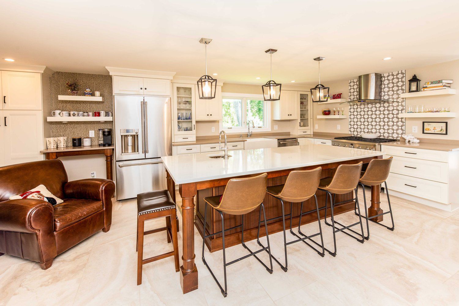 A kitchen with a large island, stools, a chair and a refrigerator.