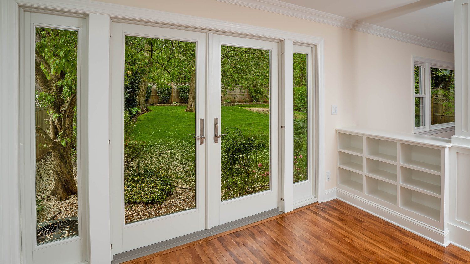 An empty room with hardwood floors and sliding glass doors leading to a backyard.