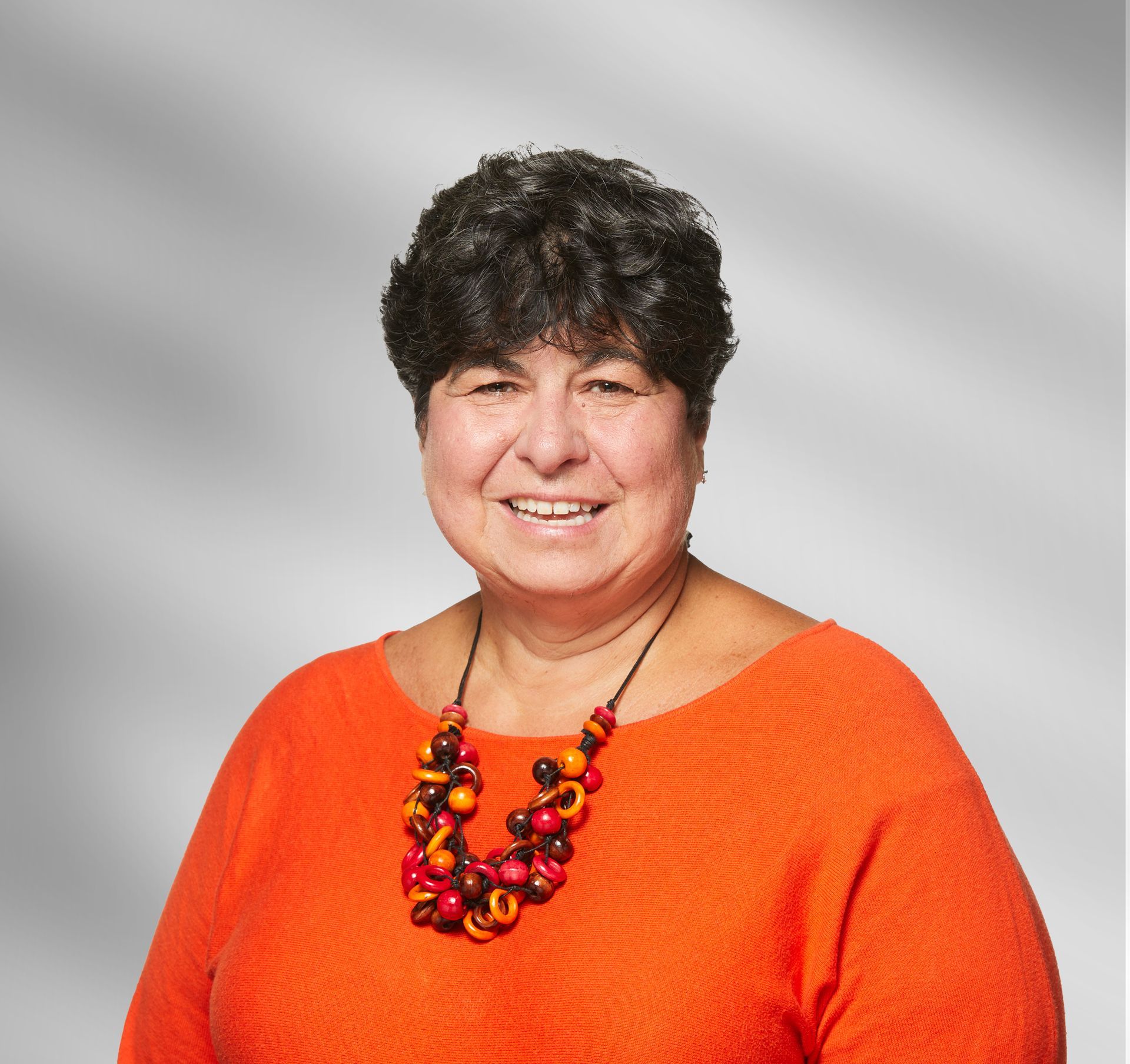 A woman wearing an orange sweater and a necklace is smiling for the camera.