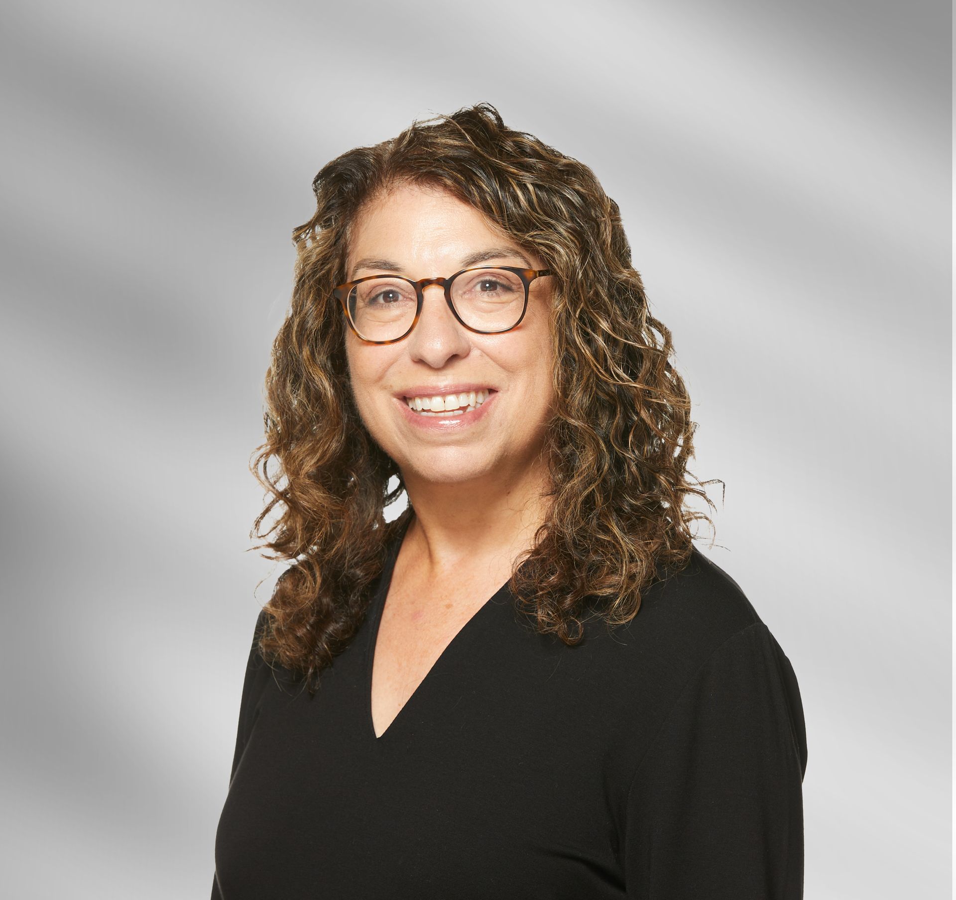 A woman wearing glasses and a black shirt is smiling.