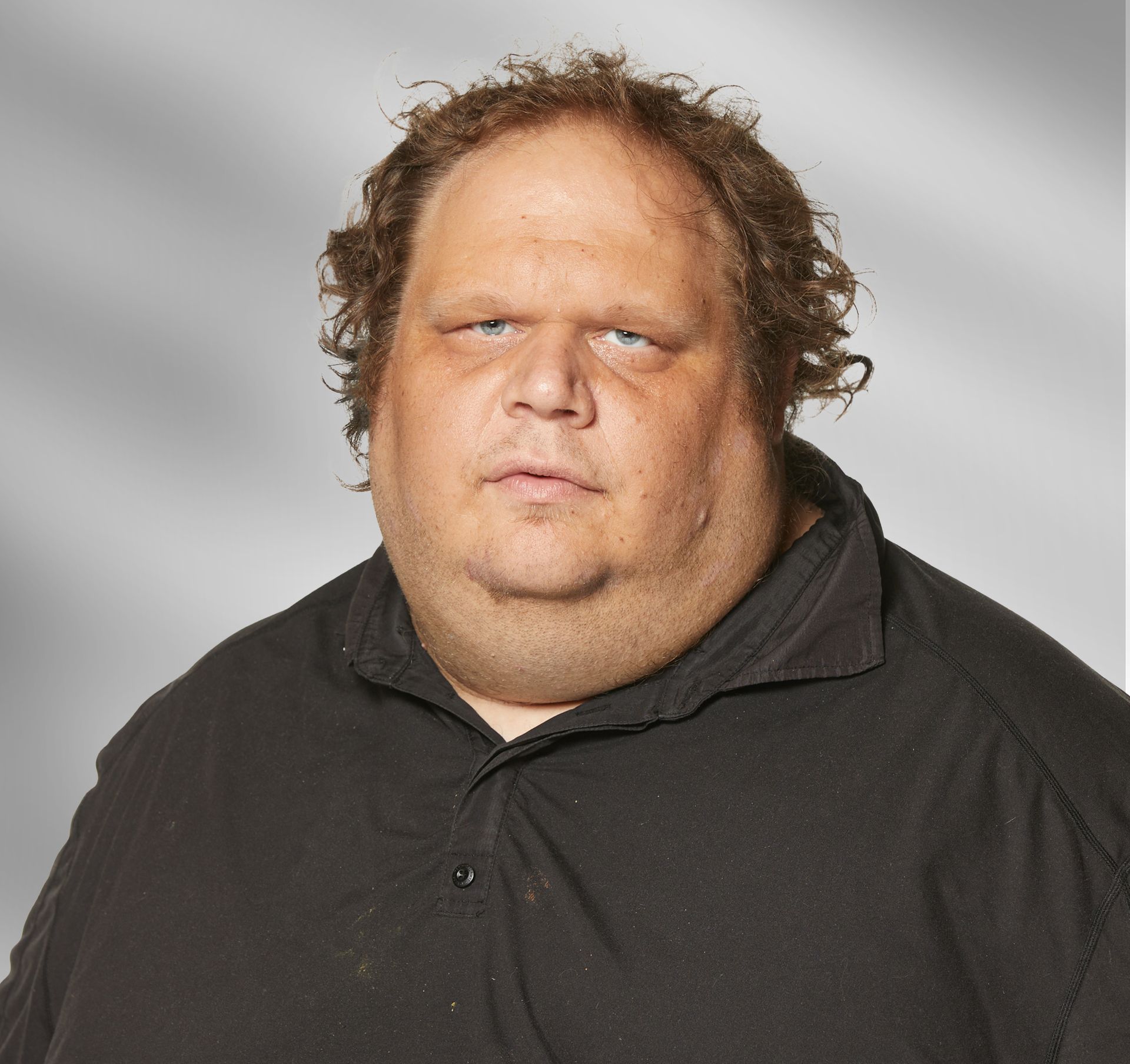 A man with curly hair and a very large neck is wearing a black shirt