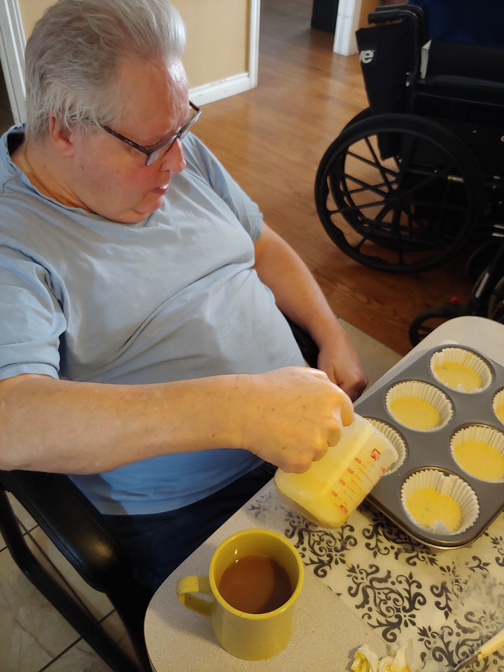 a man in a wheelchair pours liquid from a cup into a muffin baking tray