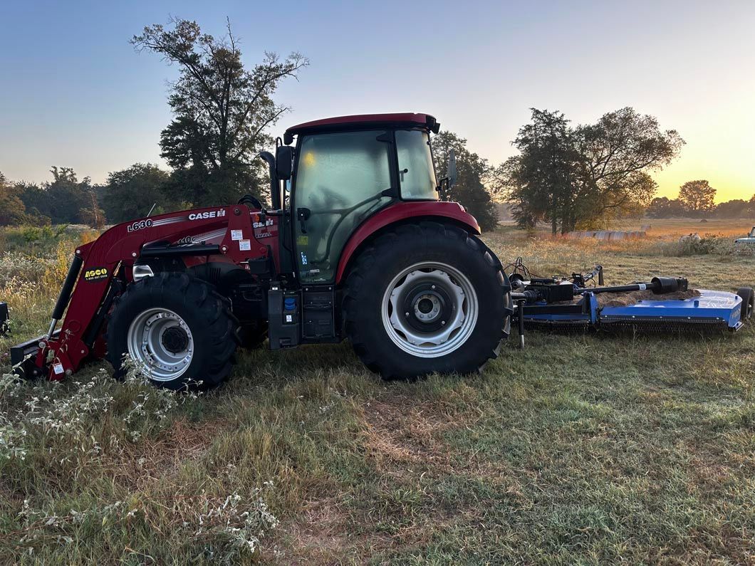 A red tractor is parked in a field with a mower attached to it.