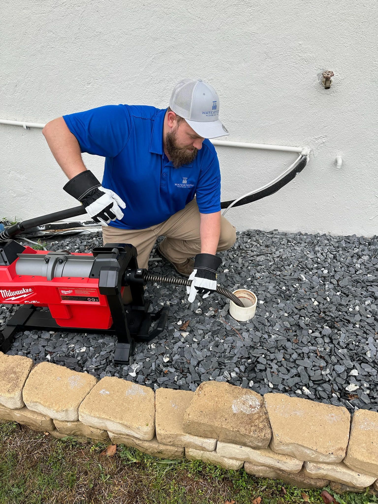 A man is kneeling down on gravel next to a machine.