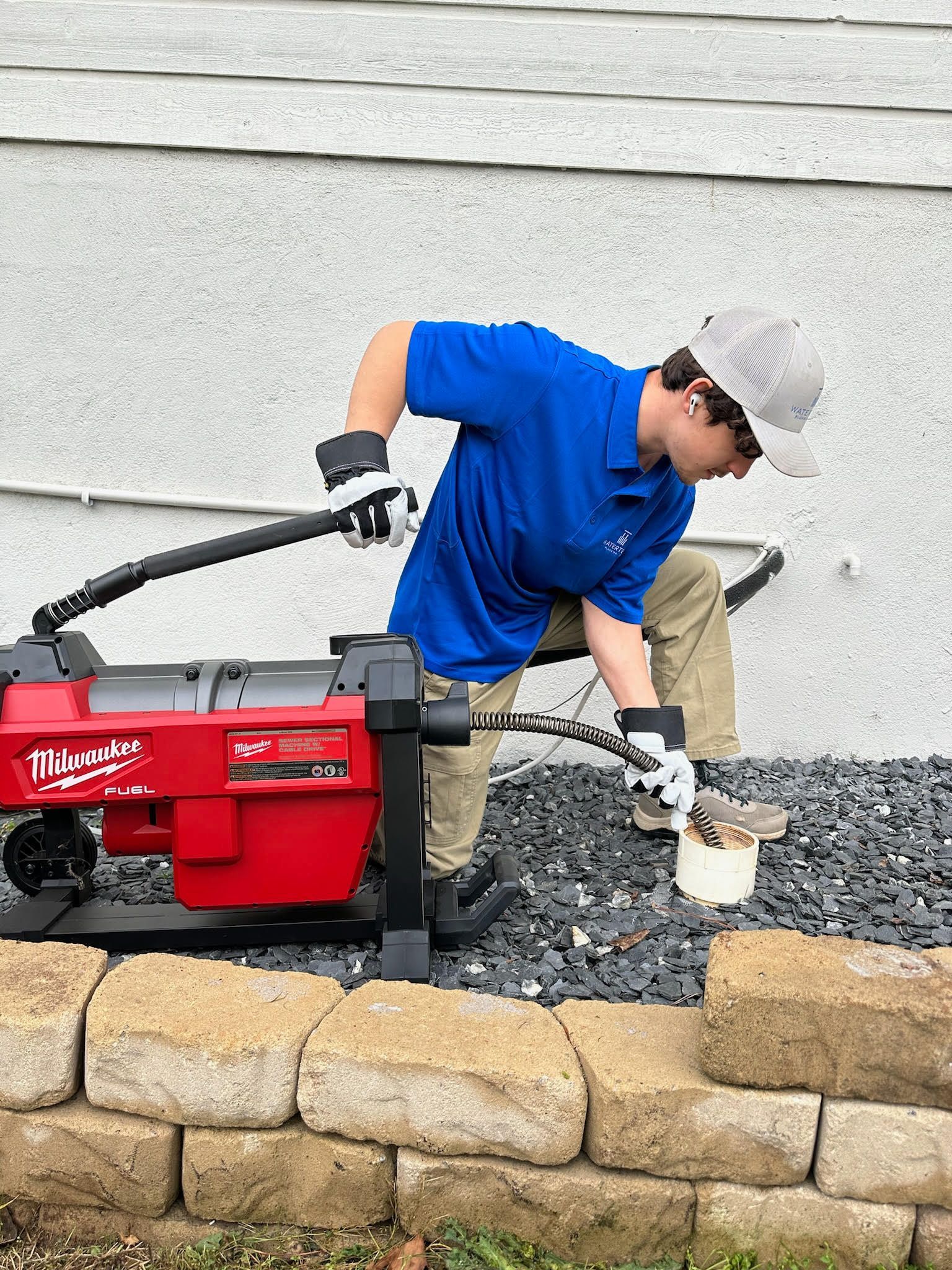 A man is using a machine to remove a drain from a brick wall.