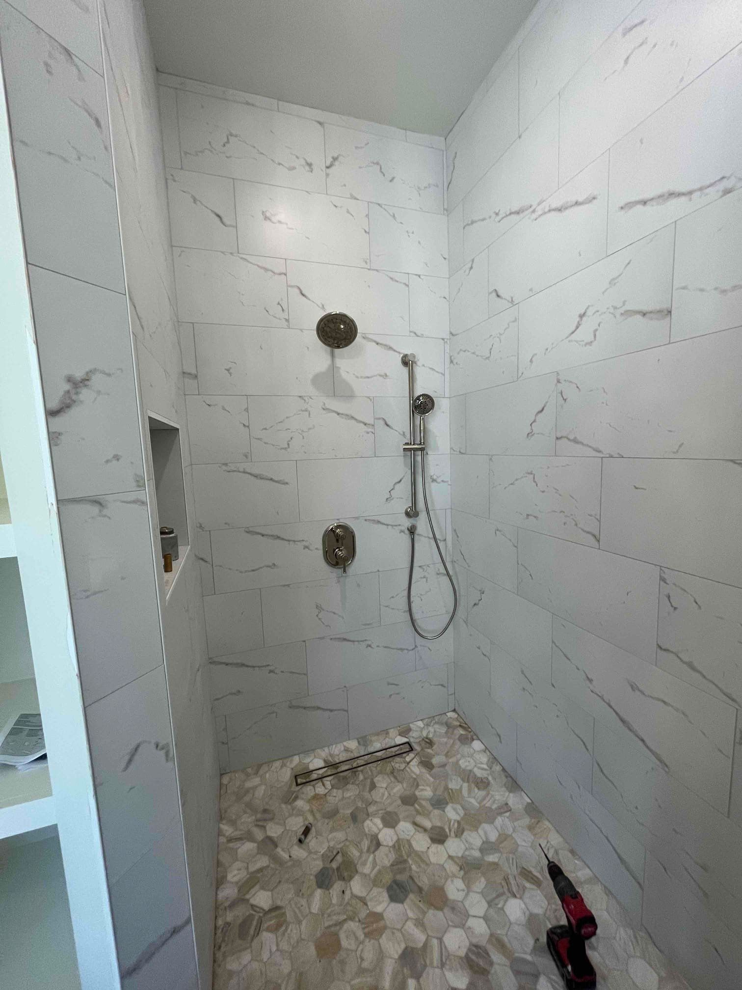 A walk in shower with marble tiles and a shower head.