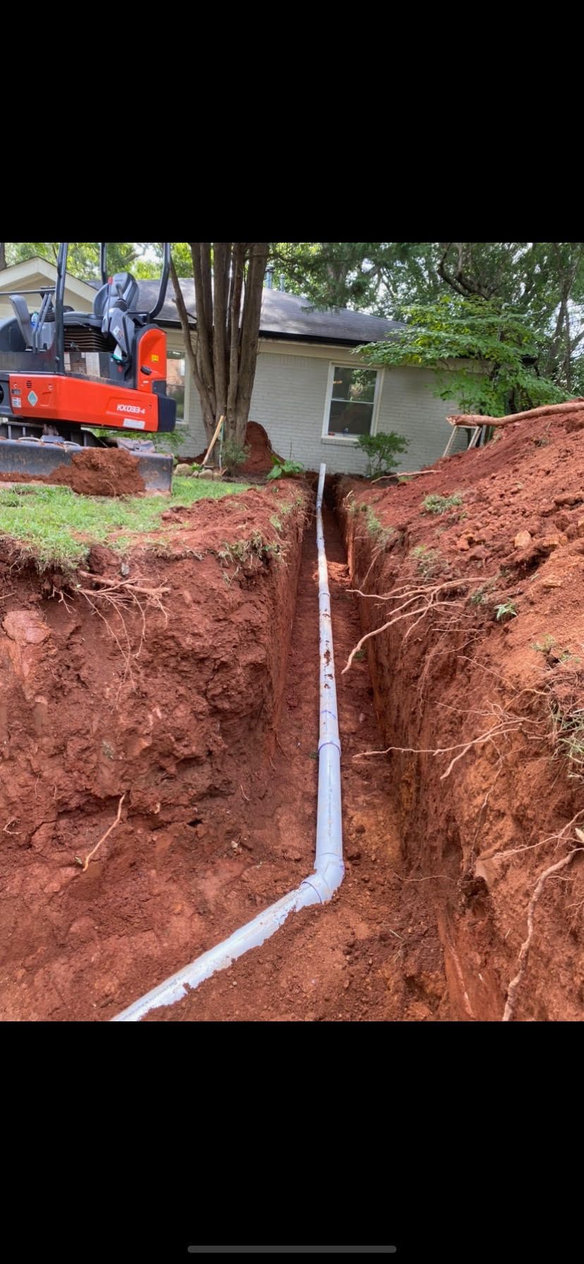 A pipe is being installed in a trench next to a house.