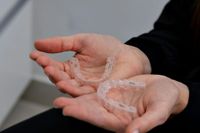Hands holding two clear dental aligners.