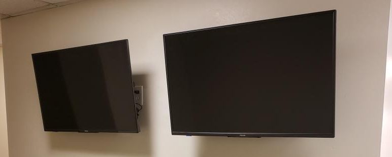 Two black flat-screen TVs mounted on a white wall.