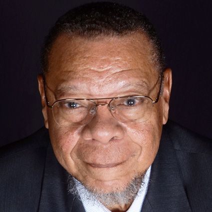 Older Black man wearing glasses, suit, and small goatee; smiling at the camera.