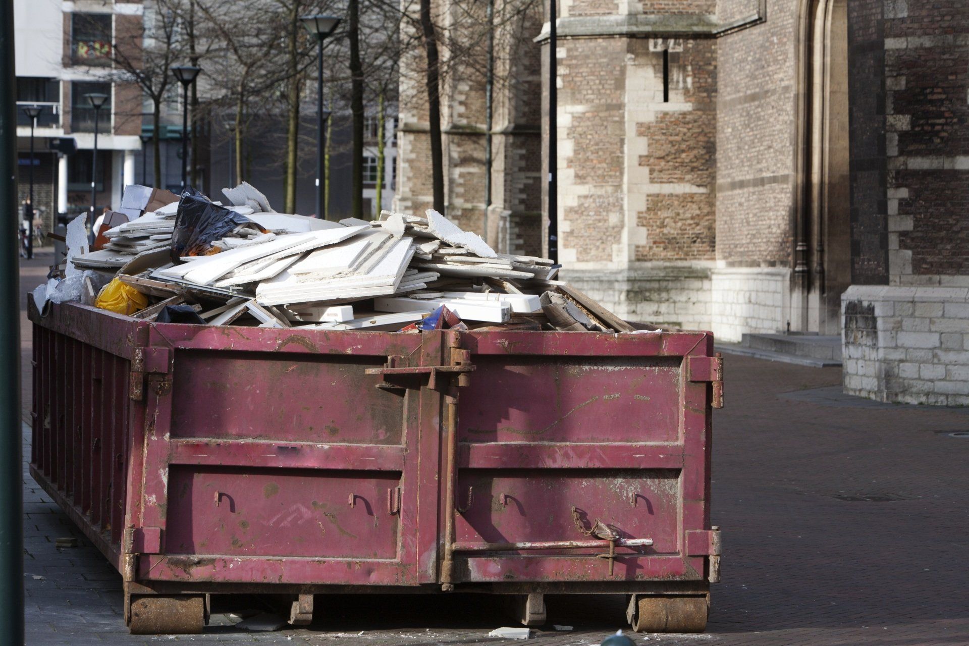 A red dumpster filled with wood is parked in front of a building.