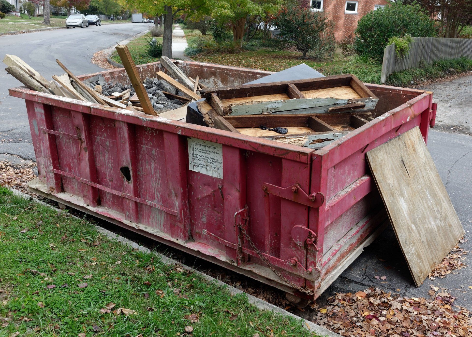 A red dumpster filled with wood is sitting on the side of the road.