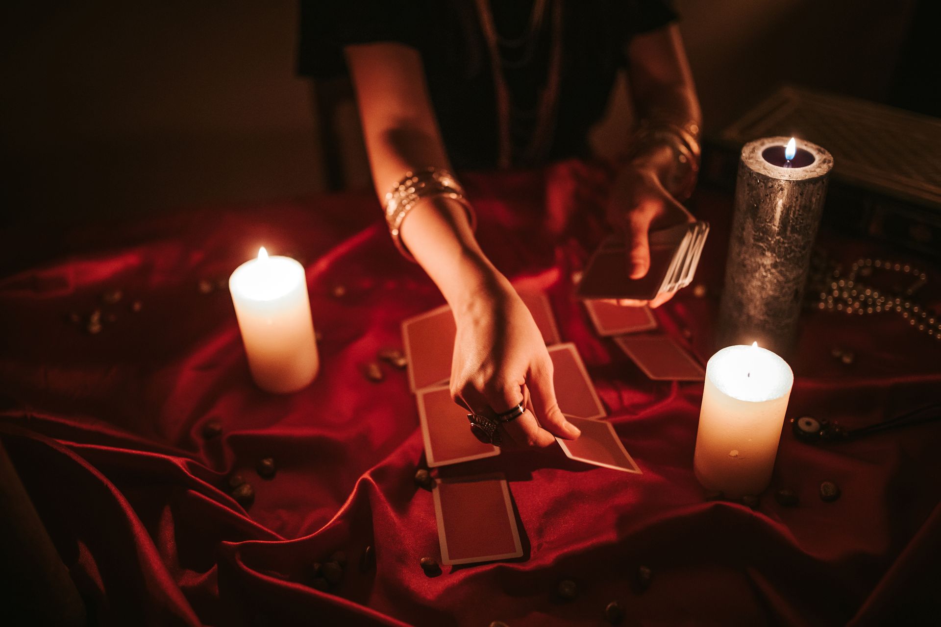 A female fortune teller reading tarot on a red velvet fabric with lighted candles. A female fortune teller reading tarot on a red velvet fabric with lighted candles.