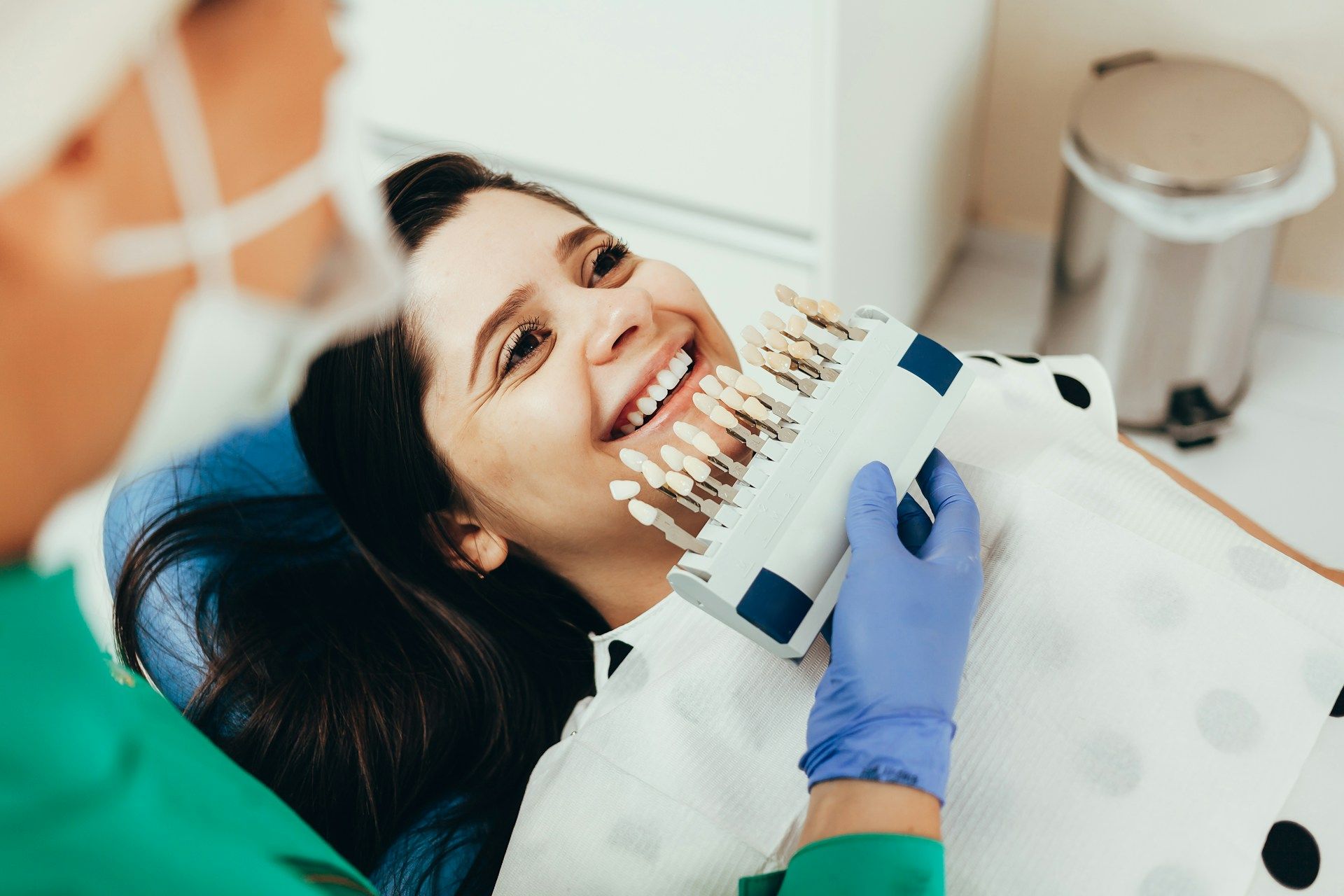 A woman is sitting in a dental chair while a dentist examines her teeth.