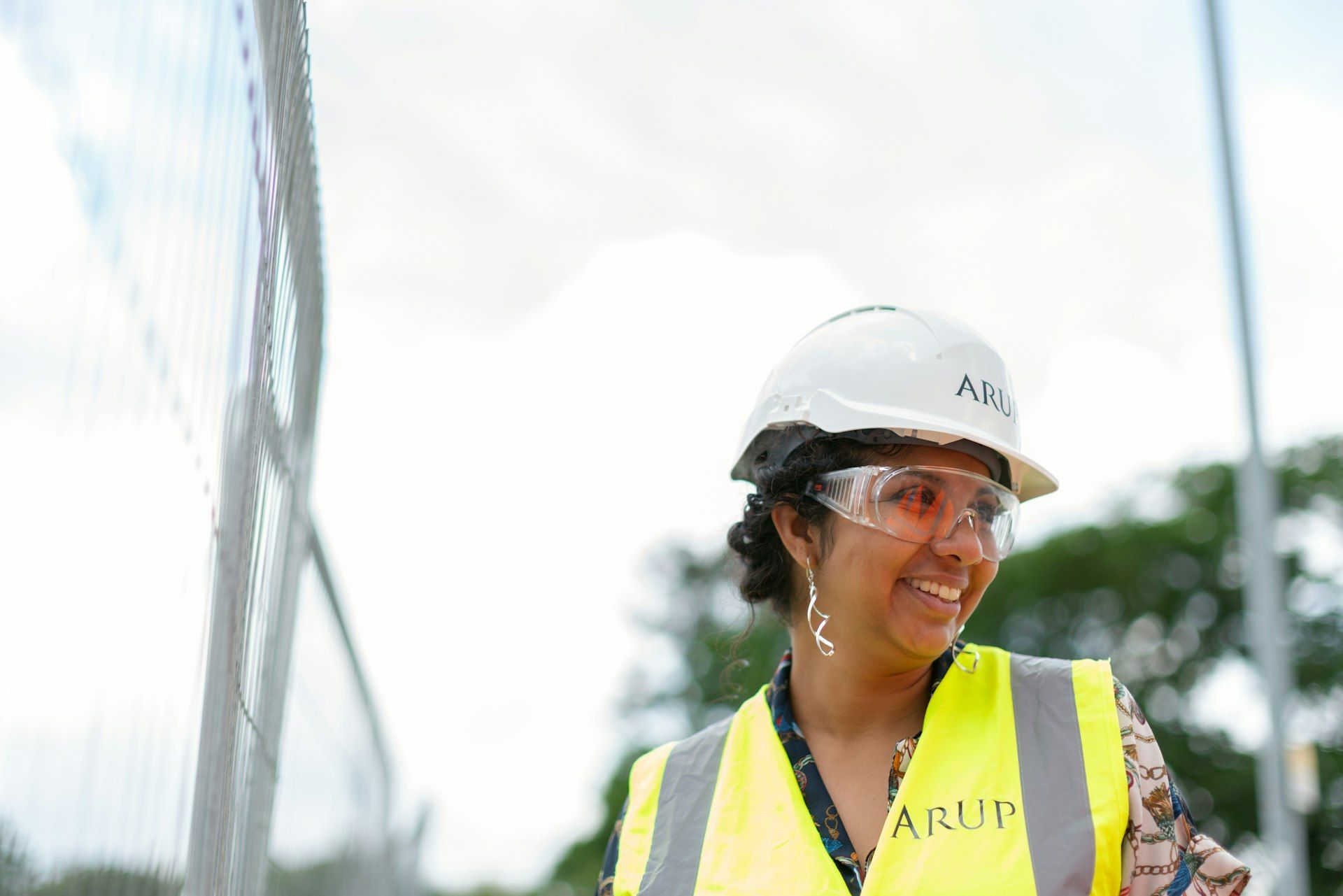 A woman wearing a hard hat and safety vest is smiling.