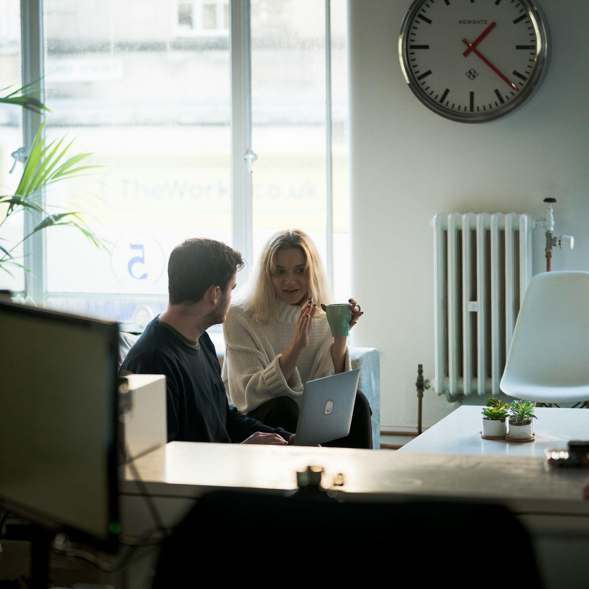 A man and a woman are sitting at a table with a clock on the wall above them
