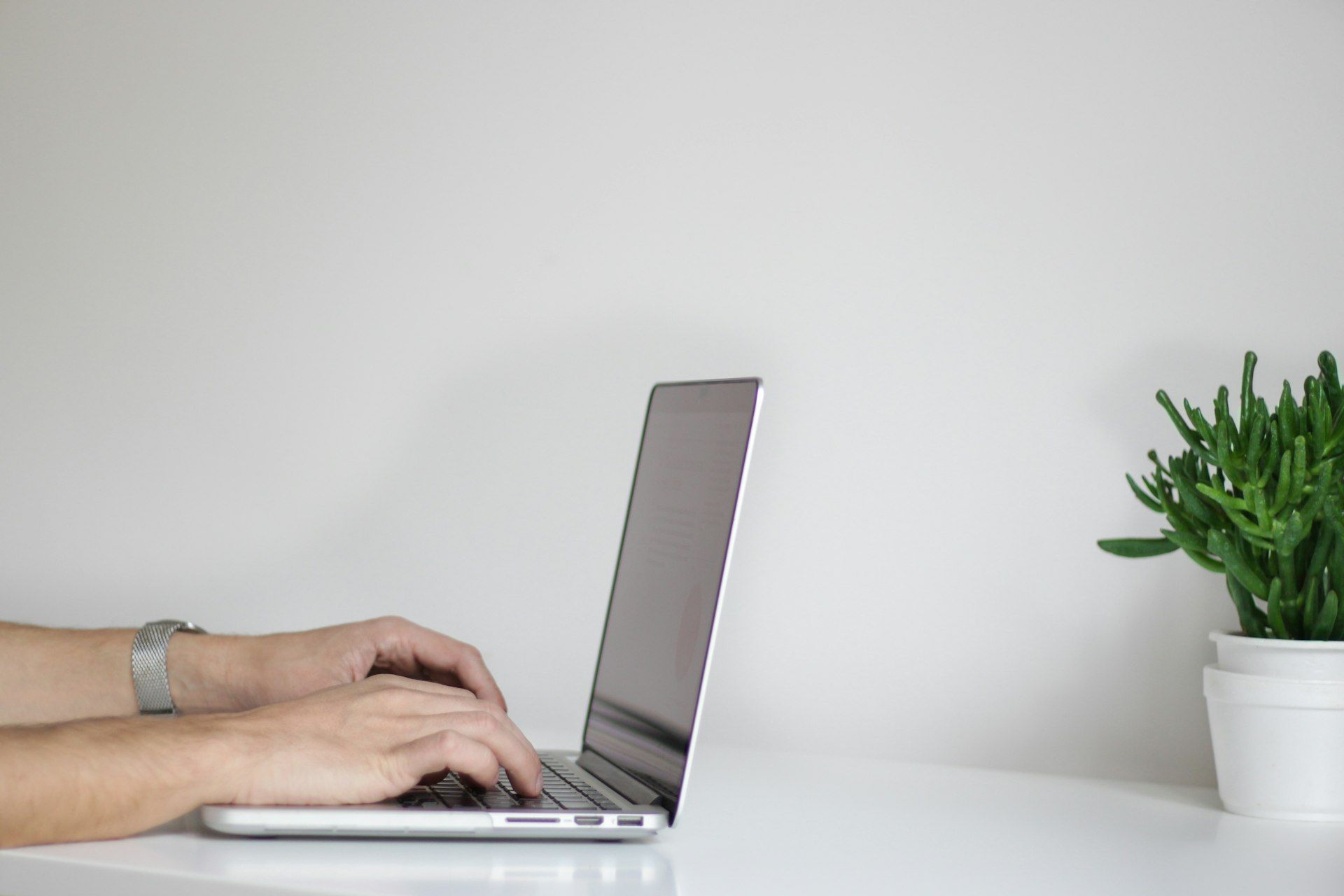 A person is typing on a laptop computer on a white table.