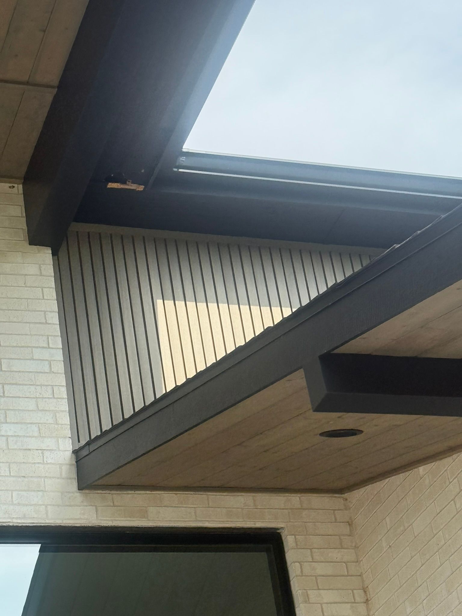 Exterior view of a modern building with a dark trim. White brick wall with a patterned panel and an angled roof.