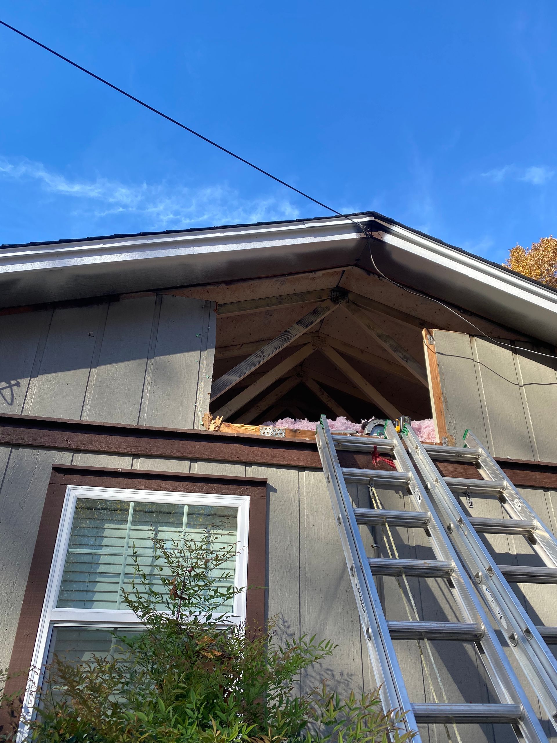 Exterior house view with open gable roof construction and ladder. Brown trim and blue sky.
