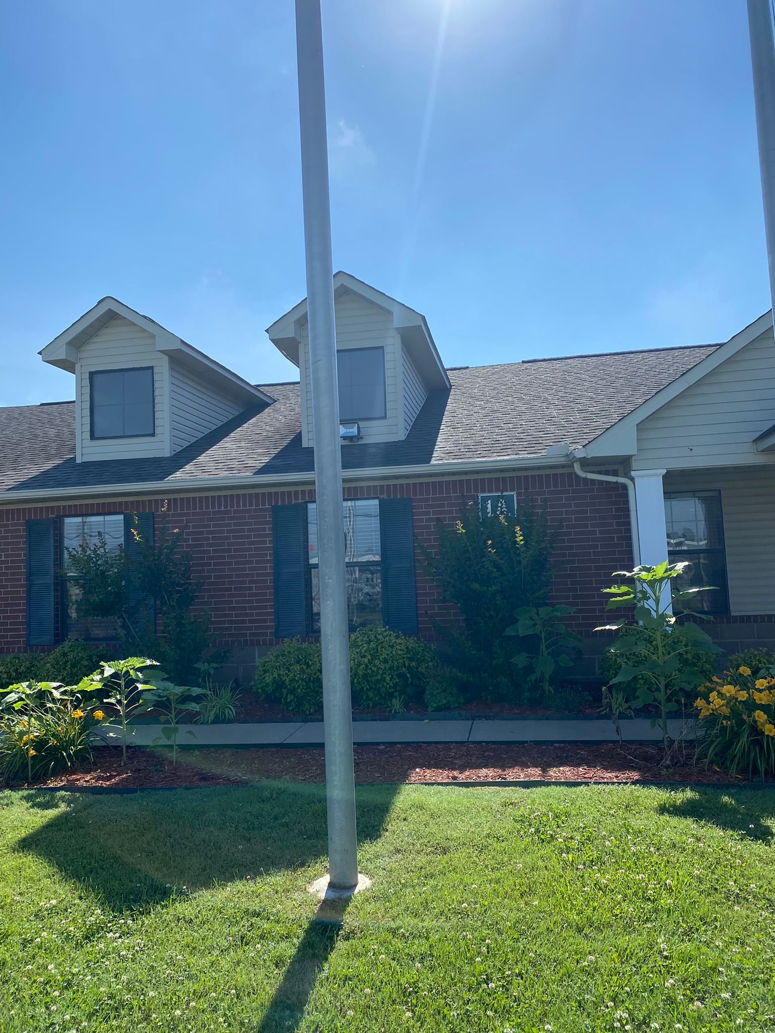 Brick house with dormers, green lawn, blue sky, and a tall pole in the foreground.