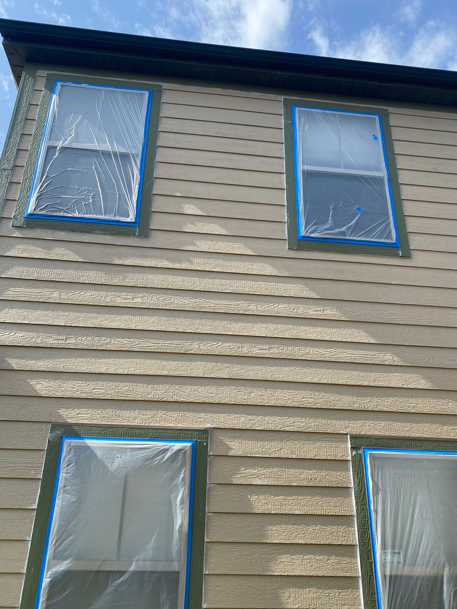 Exterior of a building with windows covered in plastic, blue tape around the frames, ready for painting.