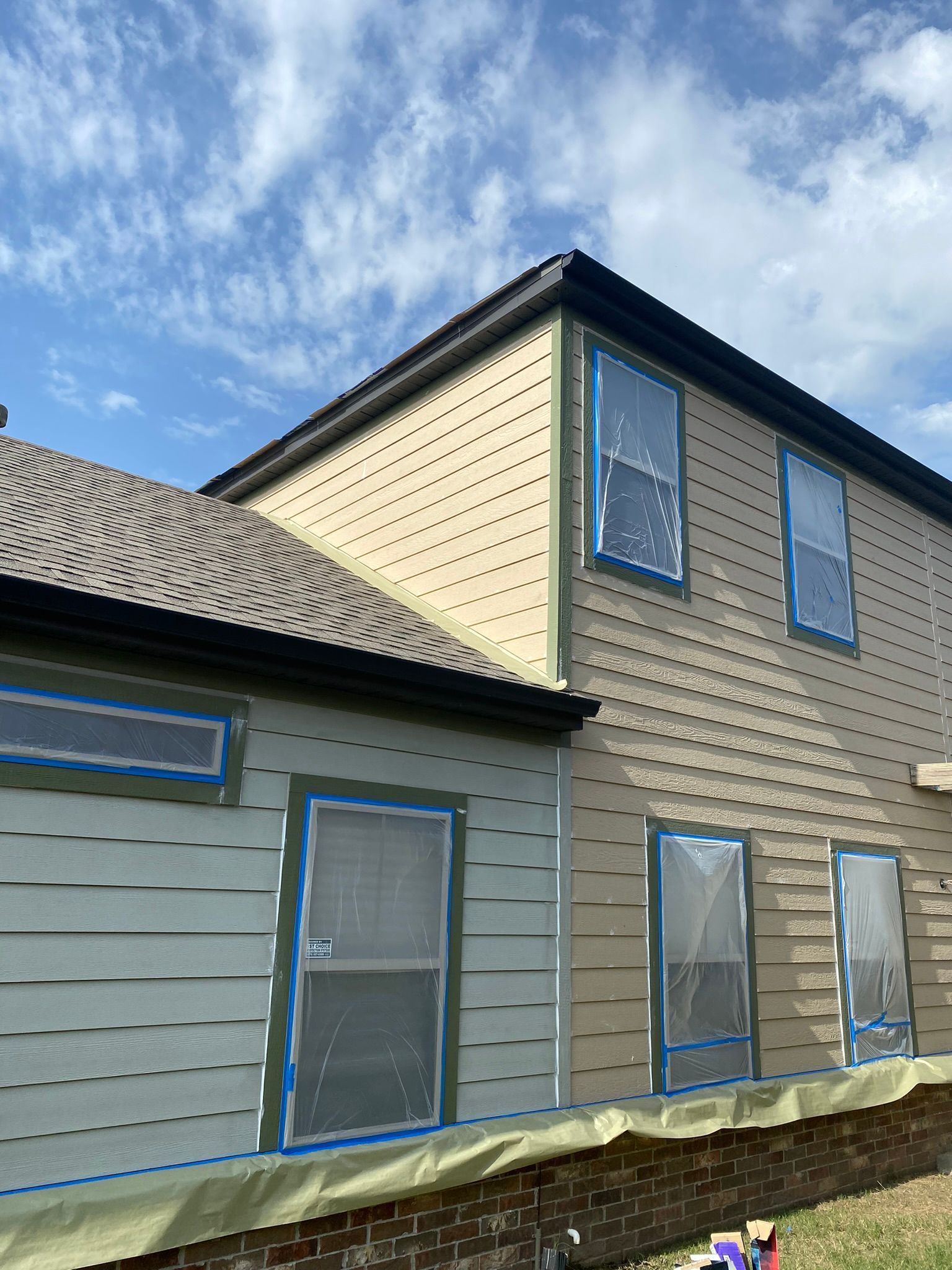 Exterior of a house with different siding colors. Windows and doors are taped off, preparing for painting.