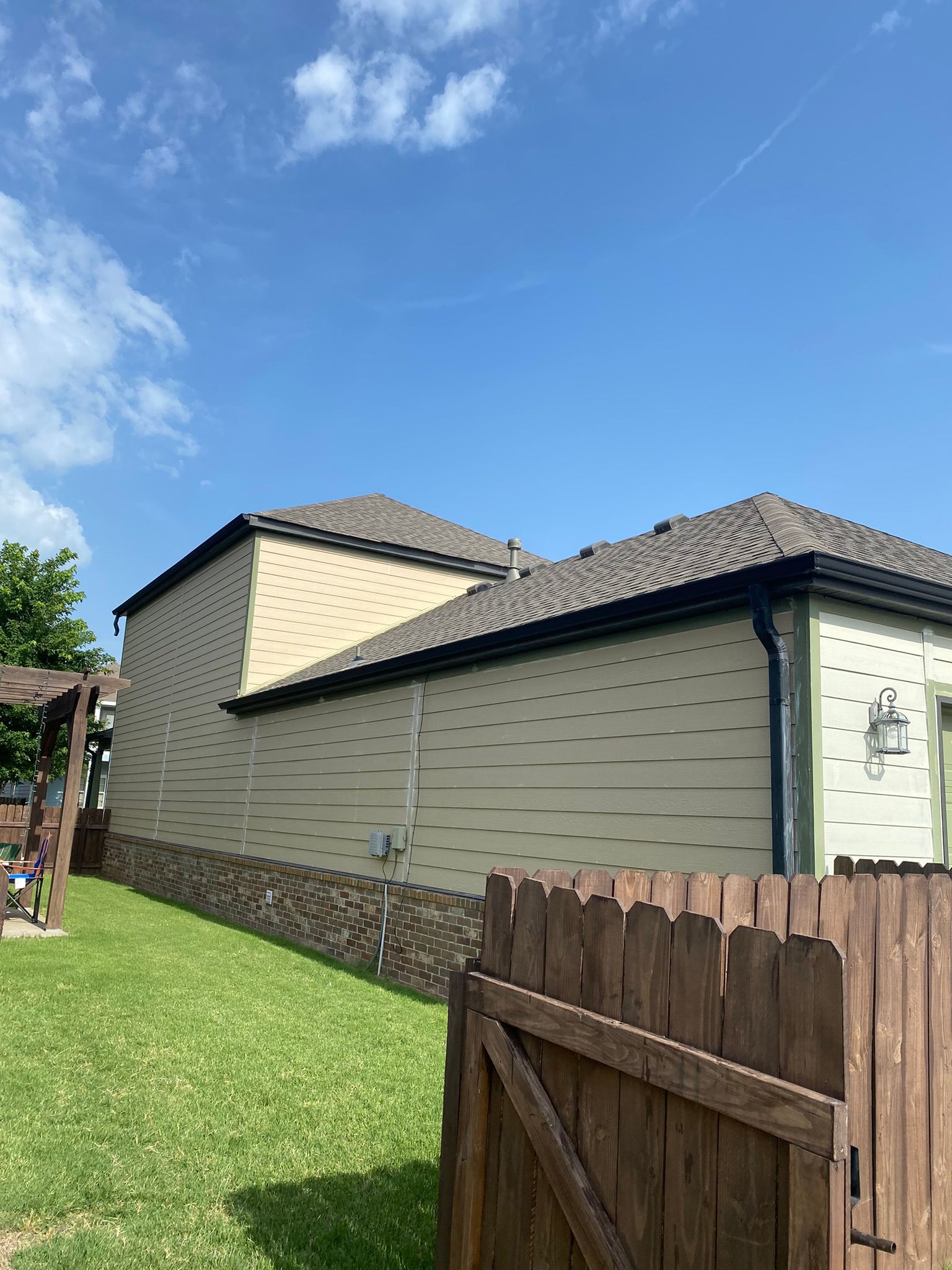 Tan siding on a building with a brown roof and a wooden fence in the foreground against a blue sky.