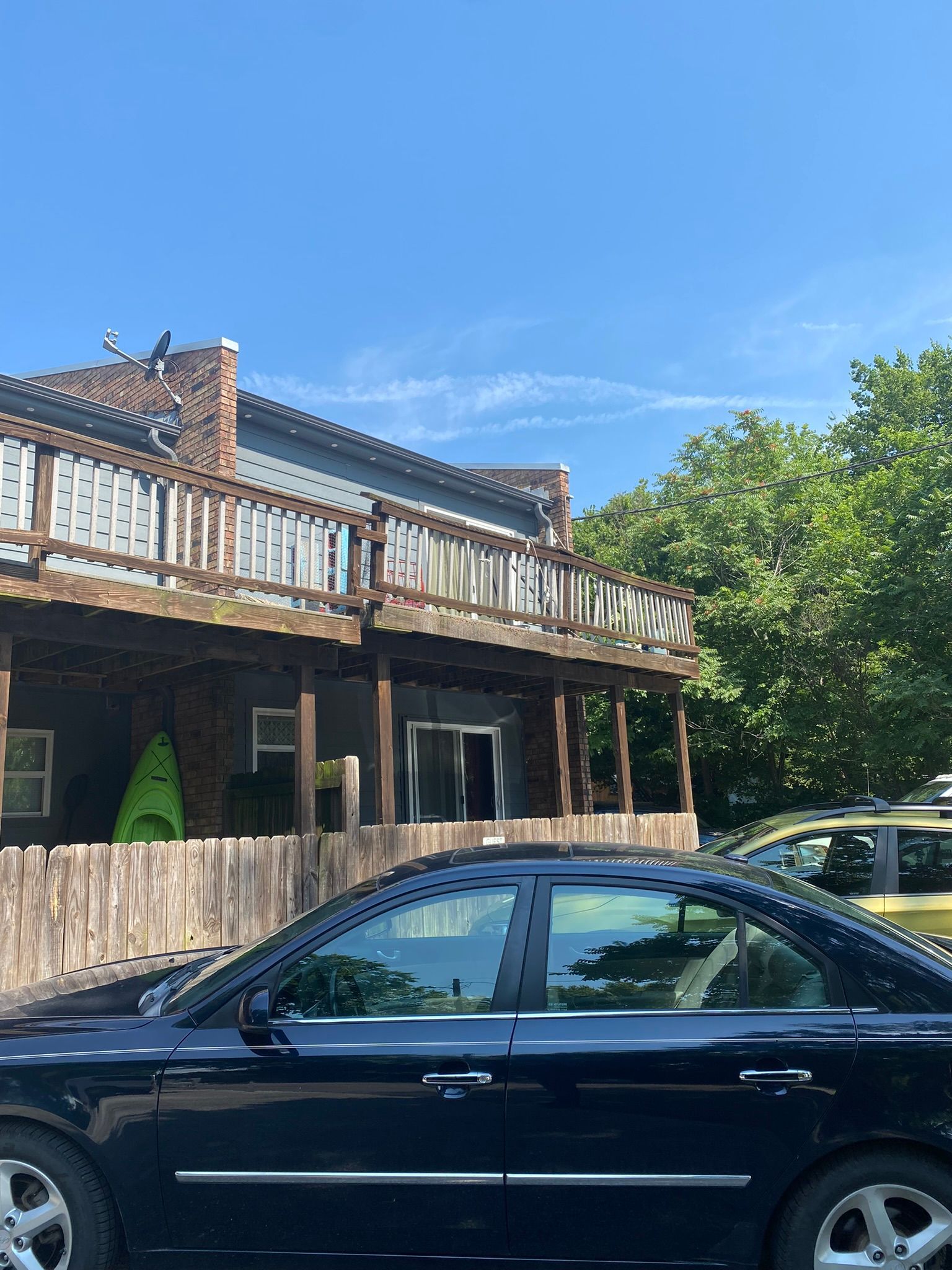 Black car parked in front of a house with a wooden deck and green kayak. Blue sky.