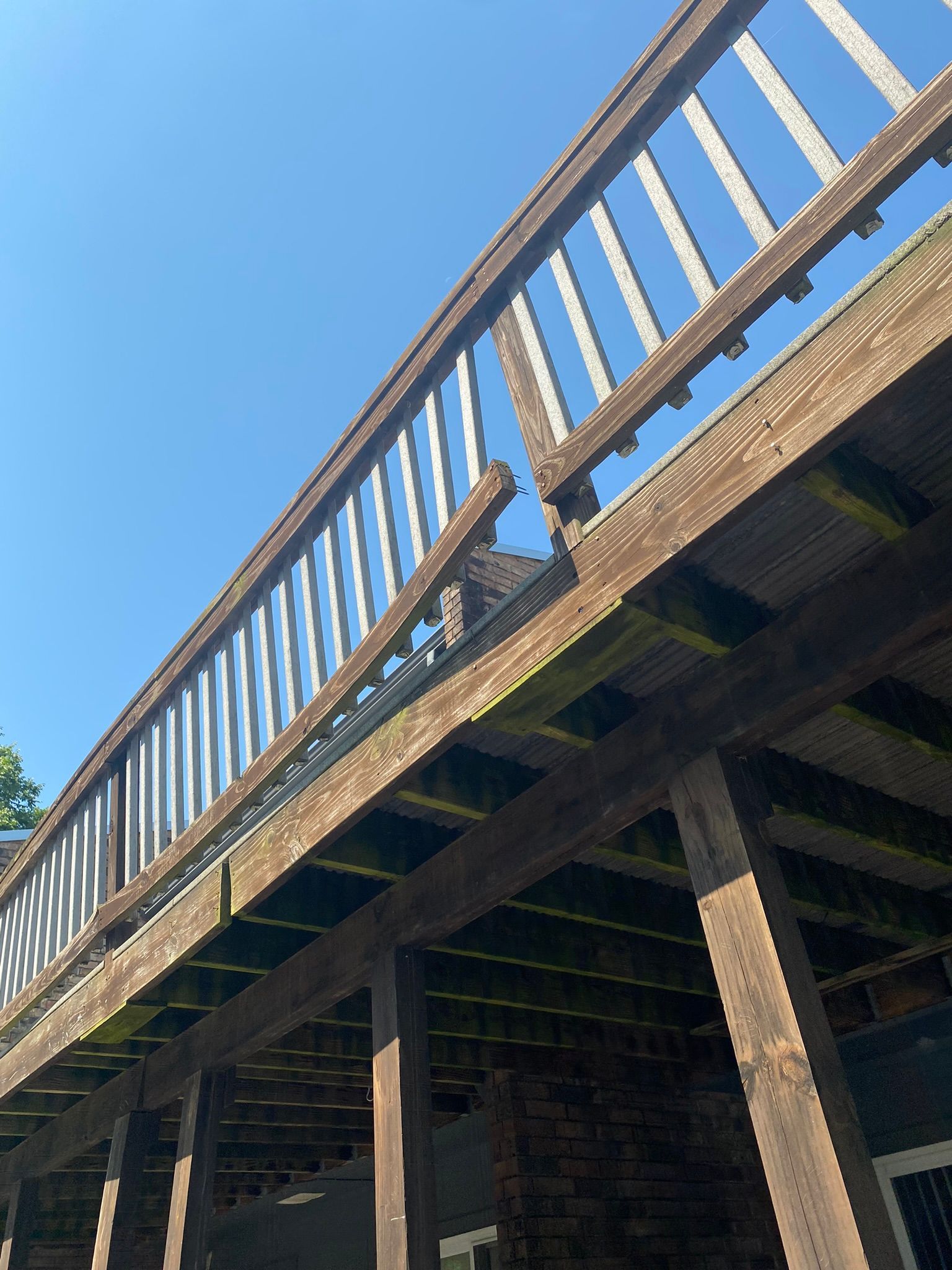 Low-angle view of a weathered wooden deck with a damaged railing against a blue sky.