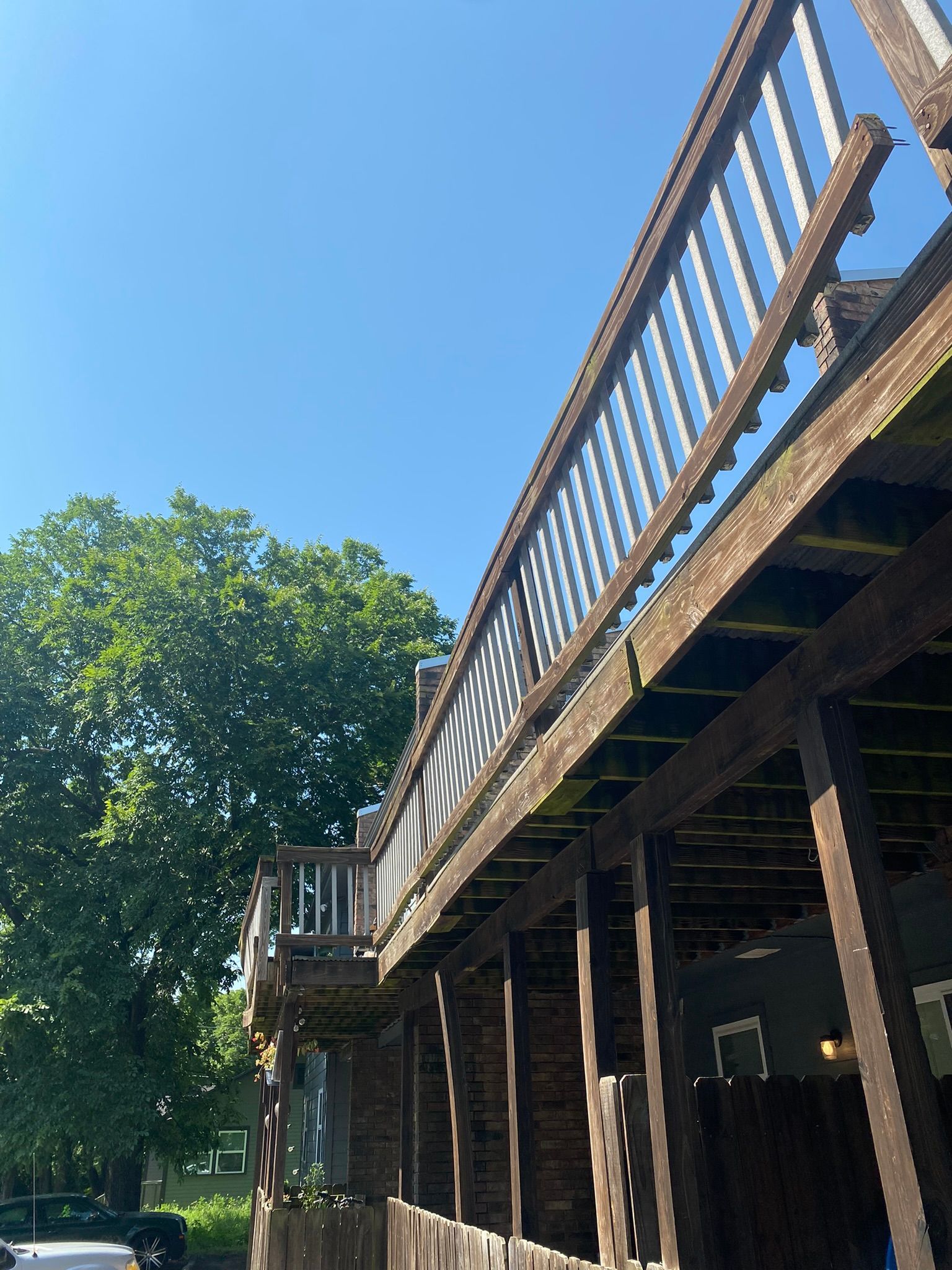 Low angle view of a weathered wooden deck with white railing, against a clear blue sky, next to a brick building.