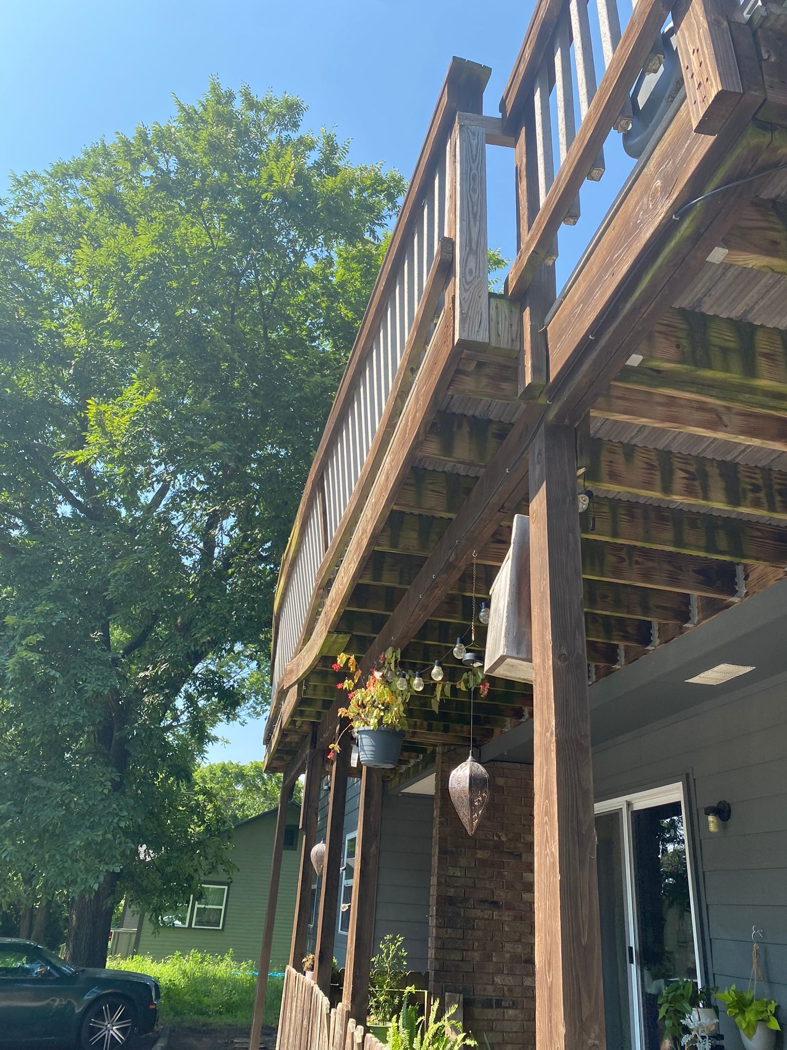 Wooden deck of a house with hanging flower baskets; a tree is on the left.