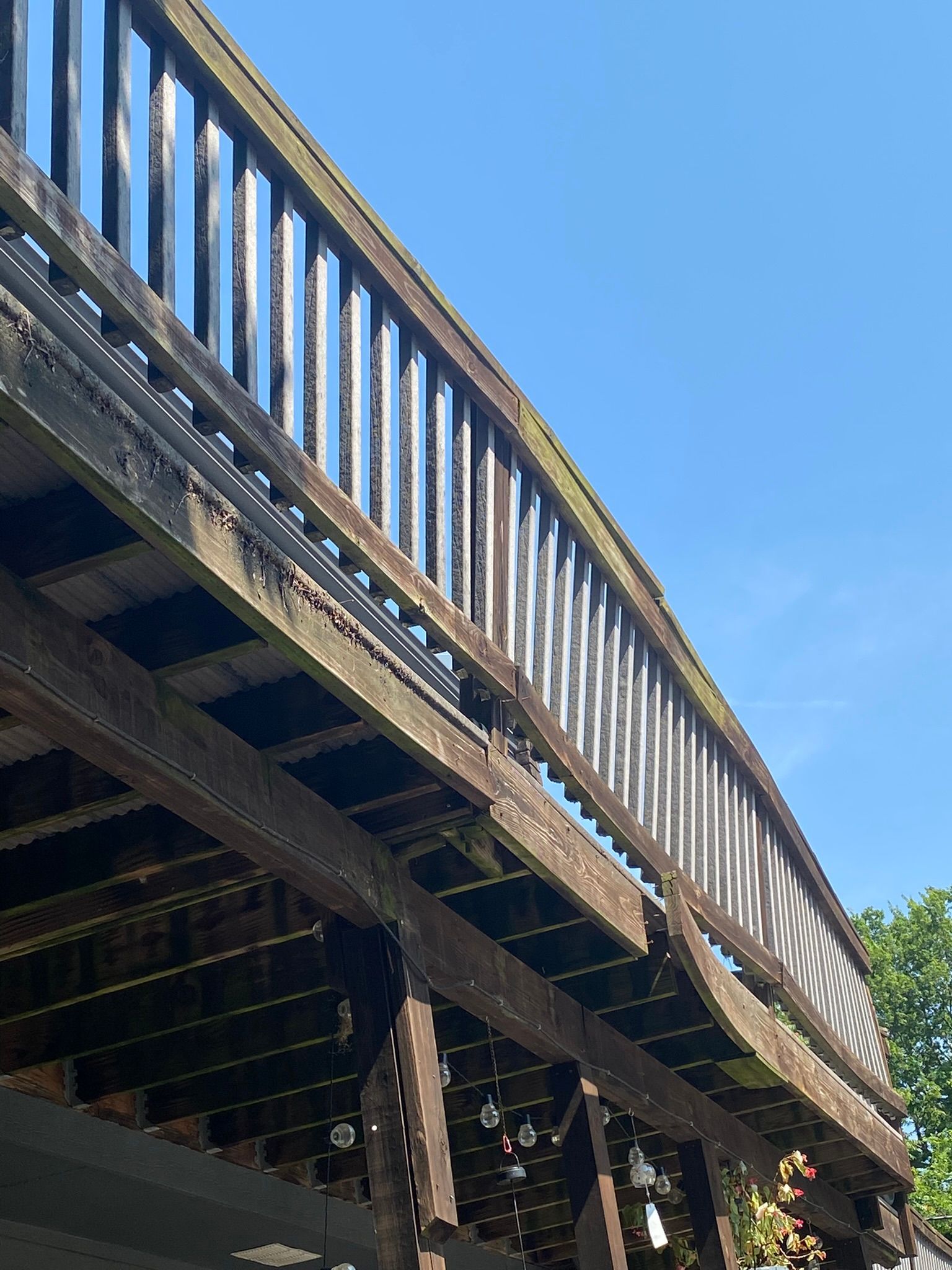 Wooden deck, viewed from below, with railings, against a blue sky.