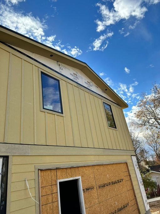 Two-story building exterior with vertical siding, windows, and blue sky.