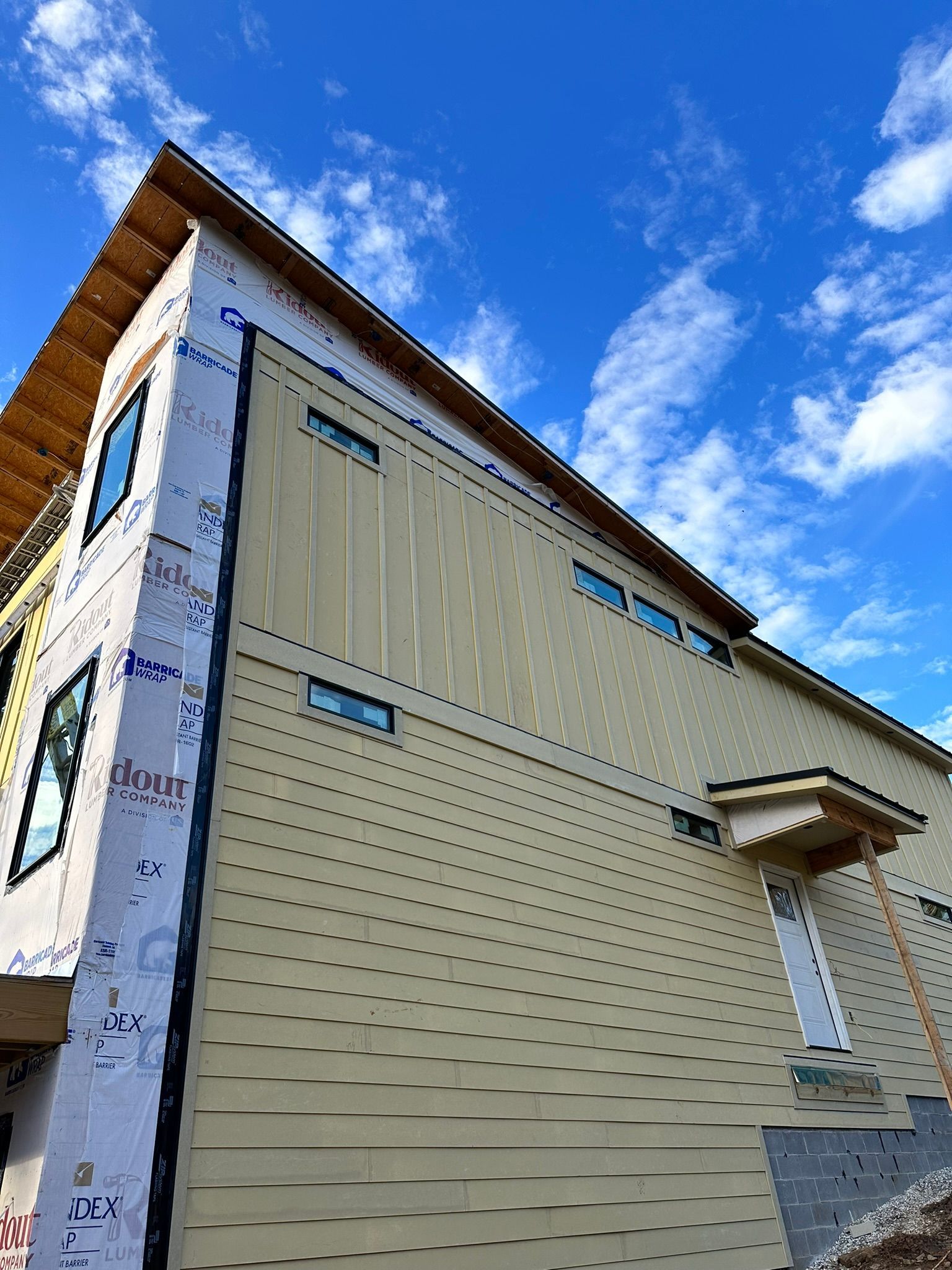 Exterior of a building under construction with light-colored siding, windows, and blue sky background.
