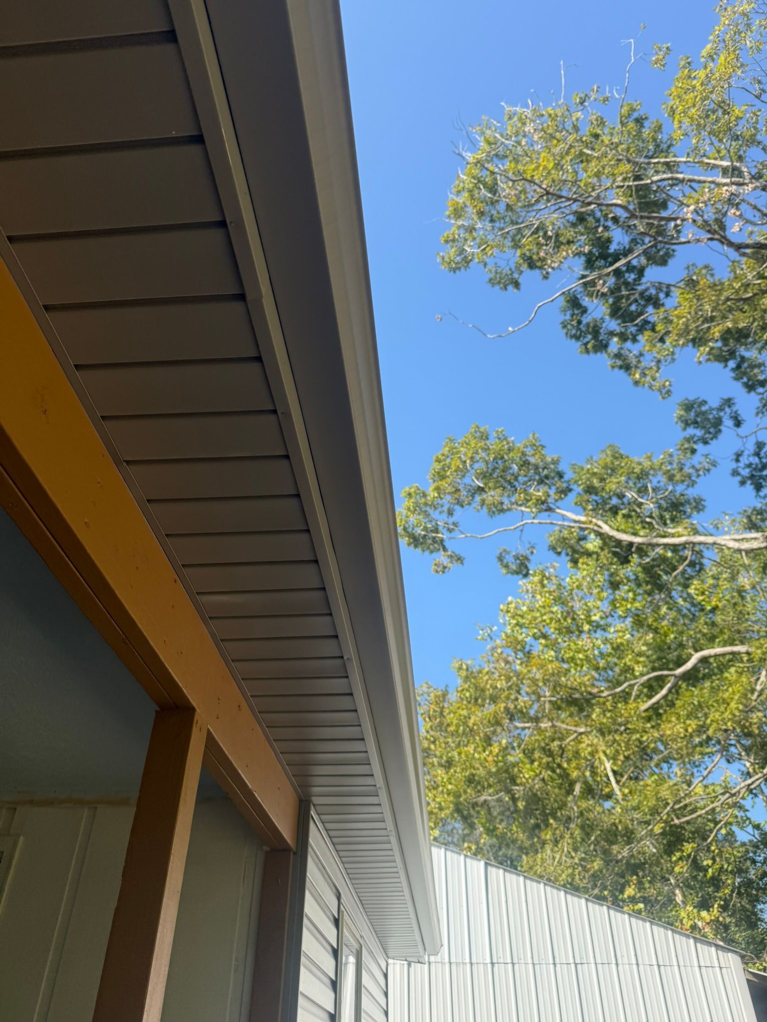 Exterior of a building with light gray siding, dark gray eaves, and a blue sky with tree branches.